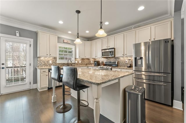 kitchen with crown molding, appliances with stainless steel finishes, a center island, light stone counters, and decorative light fixtures