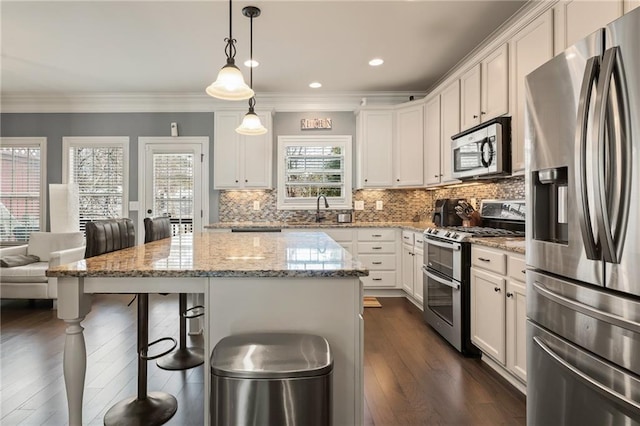 kitchen featuring pendant lighting, stainless steel appliances, light stone counters, white cabinets, and a kitchen island