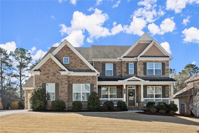 craftsman house with covered porch, a front lawn, and brick siding