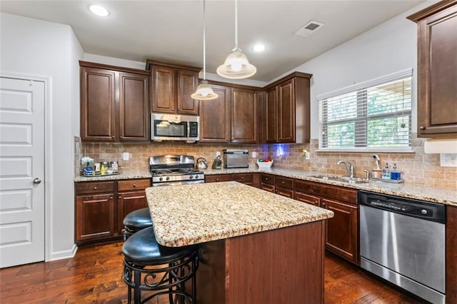 kitchen with pendant lighting, sink, appliances with stainless steel finishes, dark hardwood / wood-style floors, and a kitchen island