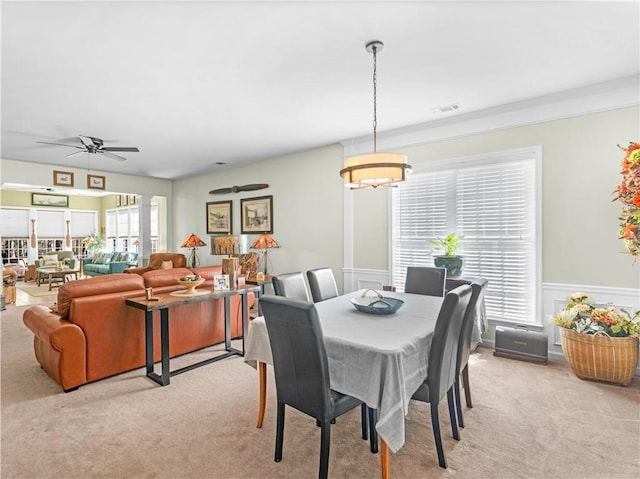 dining room featuring a ceiling fan, wainscoting, visible vents, and light colored carpet