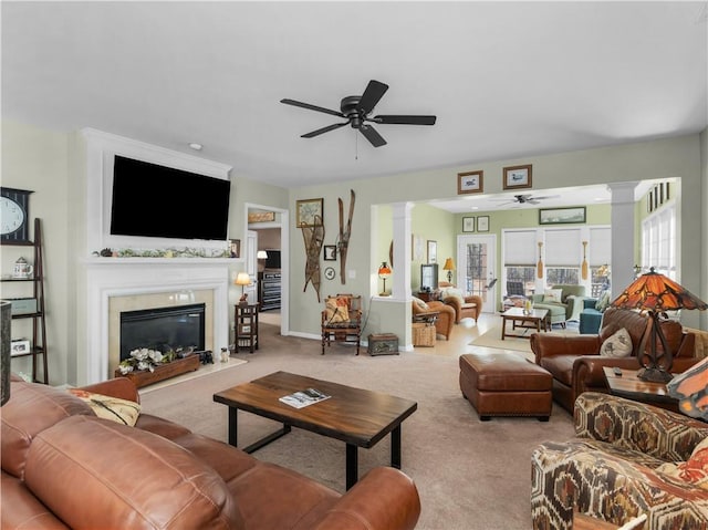 living room featuring decorative columns, baseboards, a ceiling fan, a fireplace with flush hearth, and carpet