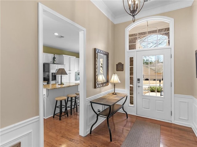 foyer entrance with ornamental molding, a chandelier, wainscoting, and wood finished floors