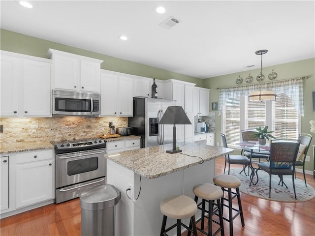 kitchen featuring visible vents, a kitchen island, appliances with stainless steel finishes, a breakfast bar area, and backsplash