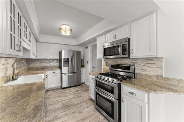 kitchen with sink, stainless steel appliances, light stone counters, ornamental molding, and white cabinets