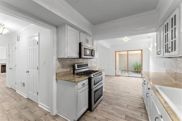 kitchen featuring sink, stainless steel appliances, light stone counters, ornamental molding, and light wood-type flooring