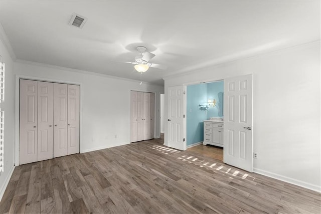 unfurnished bedroom featuring ceiling fan, ornamental molding, two closets, and light wood-type flooring