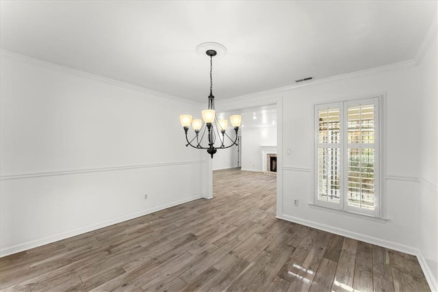 unfurnished dining area featuring hardwood / wood-style floors, crown molding, a fireplace, and a chandelier