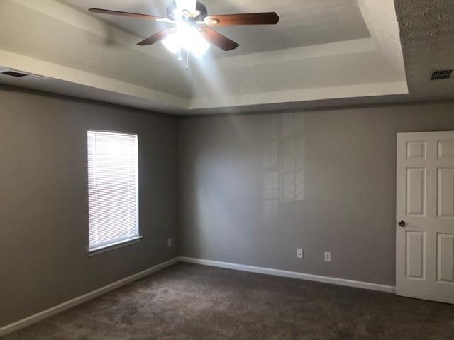 carpeted empty room featuring a raised ceiling and ceiling fan