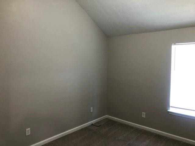 unfurnished room featuring vaulted ceiling and dark carpet