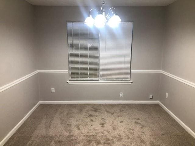 carpeted empty room featuring a notable chandelier