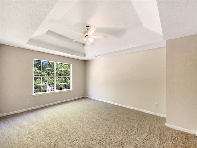 carpeted spare room featuring ceiling fan and a raised ceiling