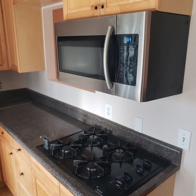 kitchen featuring light brown cabinetry, black gas stovetop, and dark stone counters