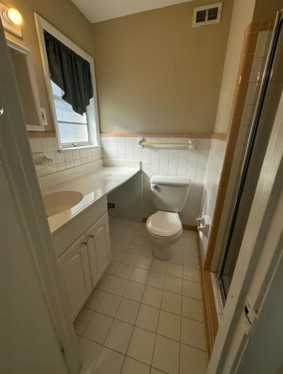 bathroom featuring tile patterned flooring, tile walls, vanity, an enclosed shower, and toilet