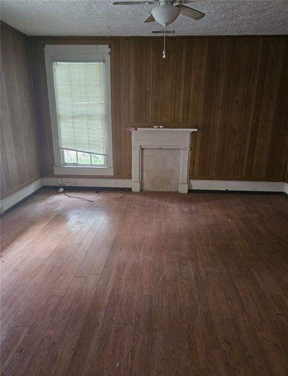 unfurnished living room with wood walls, ceiling fan, and hardwood / wood-style flooring