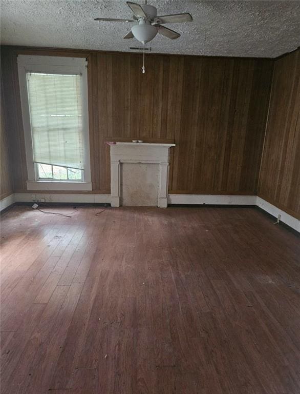 unfurnished living room featuring ceiling fan, a textured ceiling, dark hardwood / wood-style floors, and wood walls