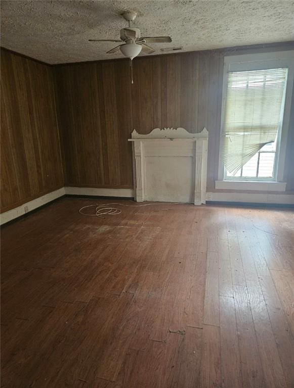 unfurnished living room with a fireplace, a textured ceiling, ceiling fan, wooden walls, and dark hardwood / wood-style floors