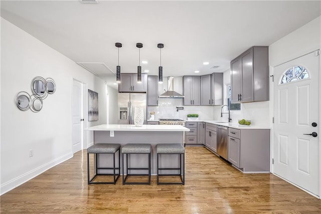 kitchen featuring stainless steel appliances, a center island, hanging light fixtures, wall chimney exhaust hood, and sink