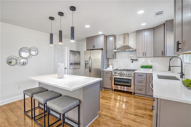 kitchen with a center island, decorative light fixtures, wall chimney range hood, stainless steel appliances, and sink