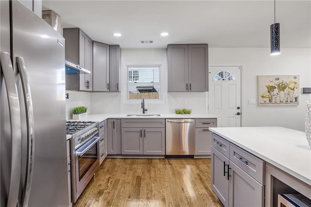 kitchen featuring stainless steel appliances, sink, hanging light fixtures, light wood-type flooring, and gray cabinetry