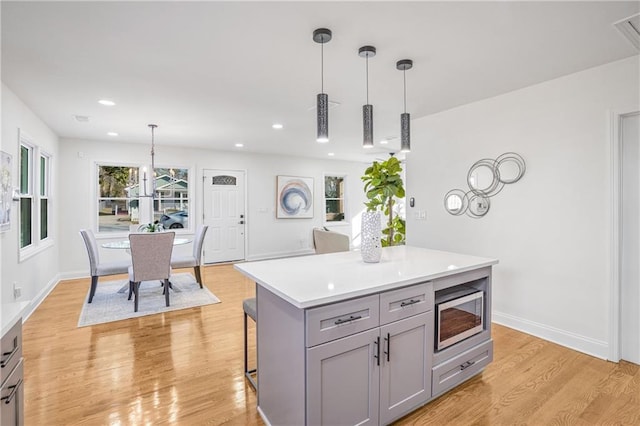 kitchen with stainless steel microwave, gray cabinets, a center island, a kitchen bar, and hanging light fixtures