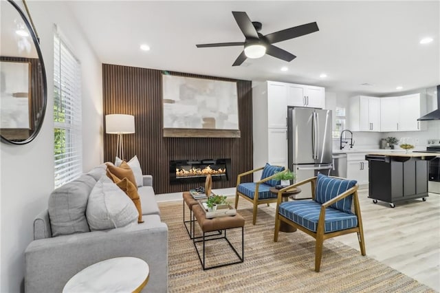 living room featuring sink, a fireplace, ceiling fan, and light hardwood / wood-style flooring