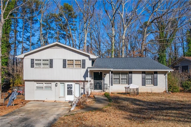 tri-level home with a shingled roof, brick siding, and driveway