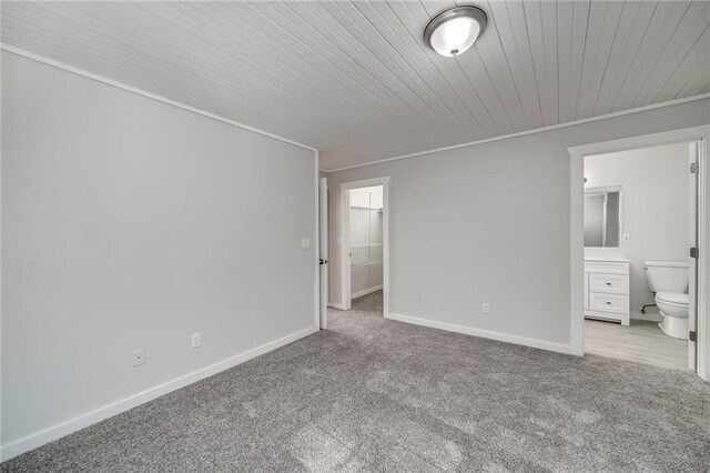 unfurnished bedroom with ensuite bathroom, wooden ceiling, light colored carpet, baseboards, and ornamental molding