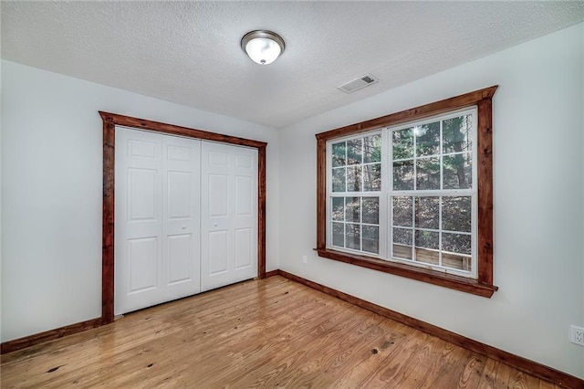 unfurnished bedroom featuring a textured ceiling, light wood-style flooring, visible vents, and baseboards