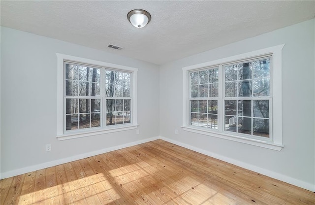 spare room featuring a textured ceiling, hardwood / wood-style floors, visible vents, and a healthy amount of sunlight