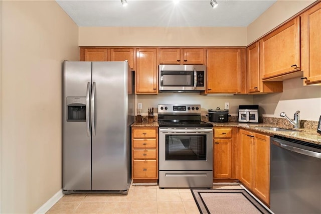 kitchen with light tile patterned flooring, sink, stainless steel appliances, and dark stone counters