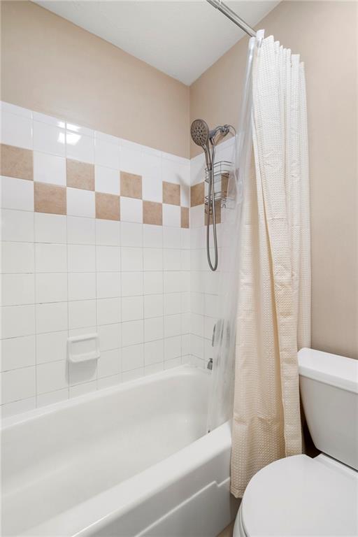 bathroom featuring toilet and shower / tub combo with curtain