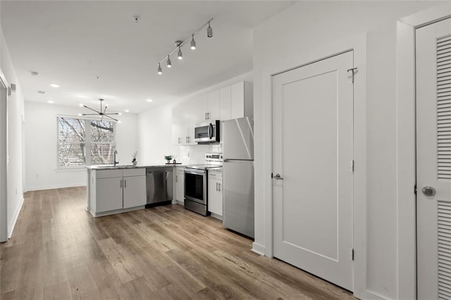 kitchen featuring baseboards, a peninsula, a sink, appliances with stainless steel finishes, and light wood-type flooring