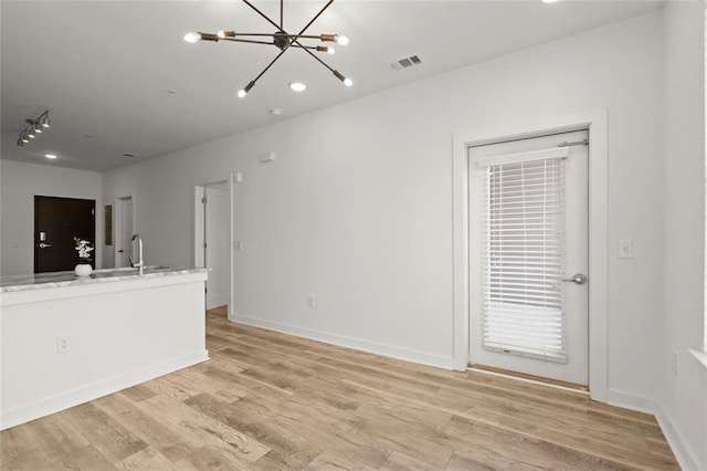 unfurnished living room featuring visible vents, baseboards, light wood-type flooring, an inviting chandelier, and a sink