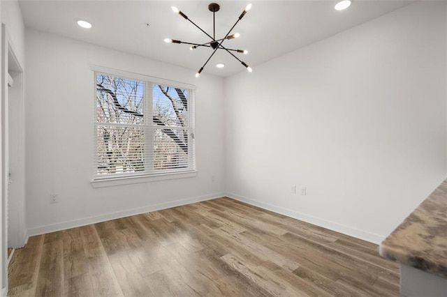 unfurnished dining area featuring recessed lighting, a chandelier, baseboards, and wood finished floors