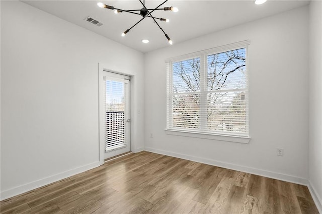 empty room featuring visible vents, an inviting chandelier, baseboards, and wood finished floors