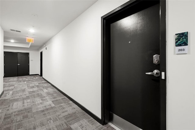 hall with a tray ceiling, visible vents, baseboards, and light carpet