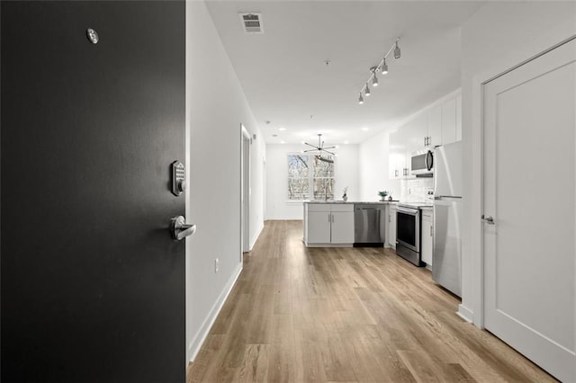 kitchen featuring visible vents, a peninsula, stainless steel appliances, white cabinetry, and light wood-type flooring