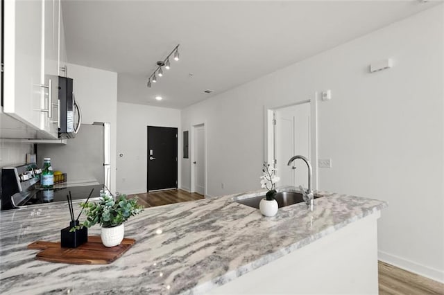 kitchen featuring a sink, stainless steel microwave, range with electric stovetop, white cabinetry, and light stone countertops