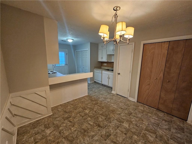 kitchen featuring a chandelier, white dishwasher, kitchen peninsula, pendant lighting, and white cabinets