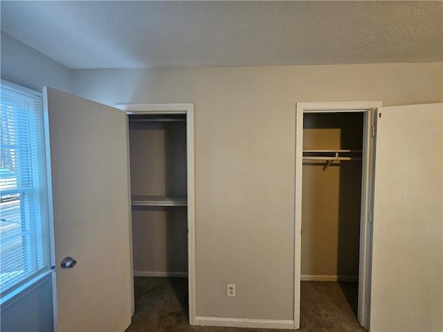 unfurnished bedroom with a spacious closet, a closet, a textured ceiling, and dark colored carpet