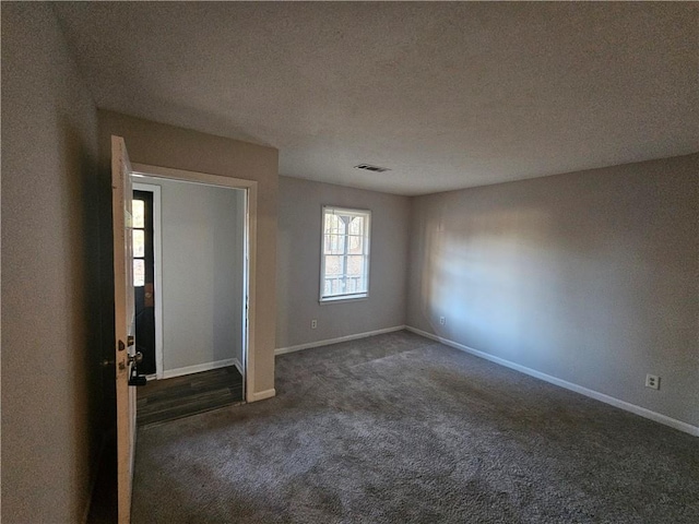 unfurnished room with a textured ceiling and dark colored carpet