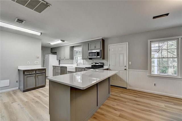 kitchen with gray cabinetry, sink, light wood-type flooring, appliances with stainless steel finishes, and a breakfast bar area