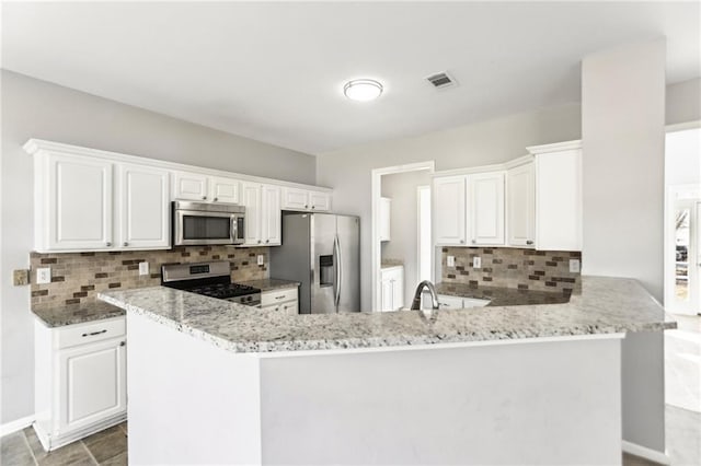 kitchen with stainless steel appliances, light stone countertops, a peninsula, and visible vents