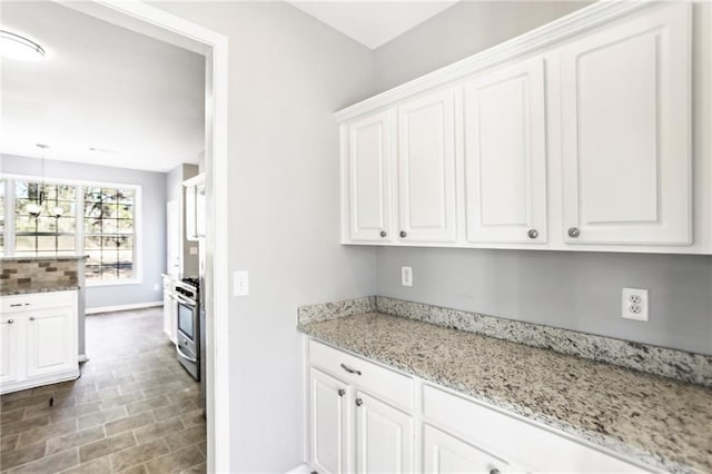 kitchen with light stone counters, baseboards, white cabinets, pendant lighting, and stainless steel gas stove