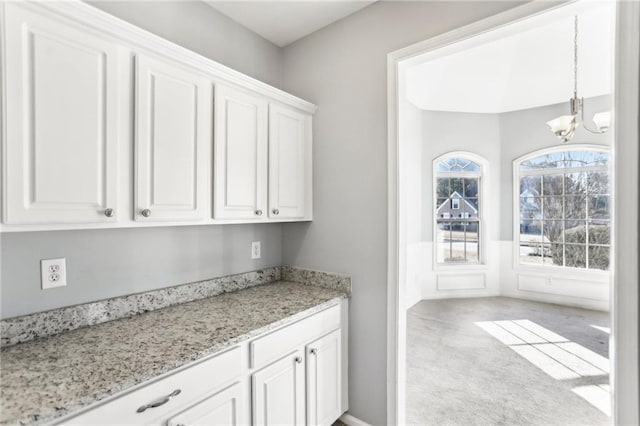 kitchen with a wainscoted wall, light stone counters, white cabinetry, carpet flooring, and a chandelier