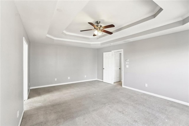 carpeted spare room featuring a tray ceiling, a ceiling fan, and baseboards