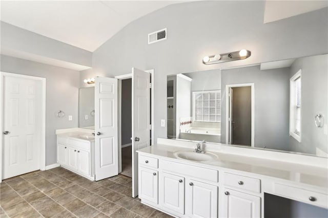 bathroom featuring vanity, lofted ceiling, a bath, and visible vents