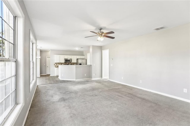 unfurnished living room featuring visible vents, light colored carpet, baseboards, and ceiling fan