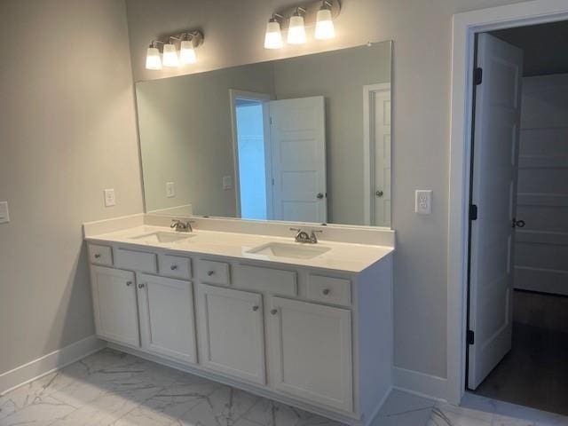 full bathroom featuring marble finish floor, double vanity, a sink, and baseboards